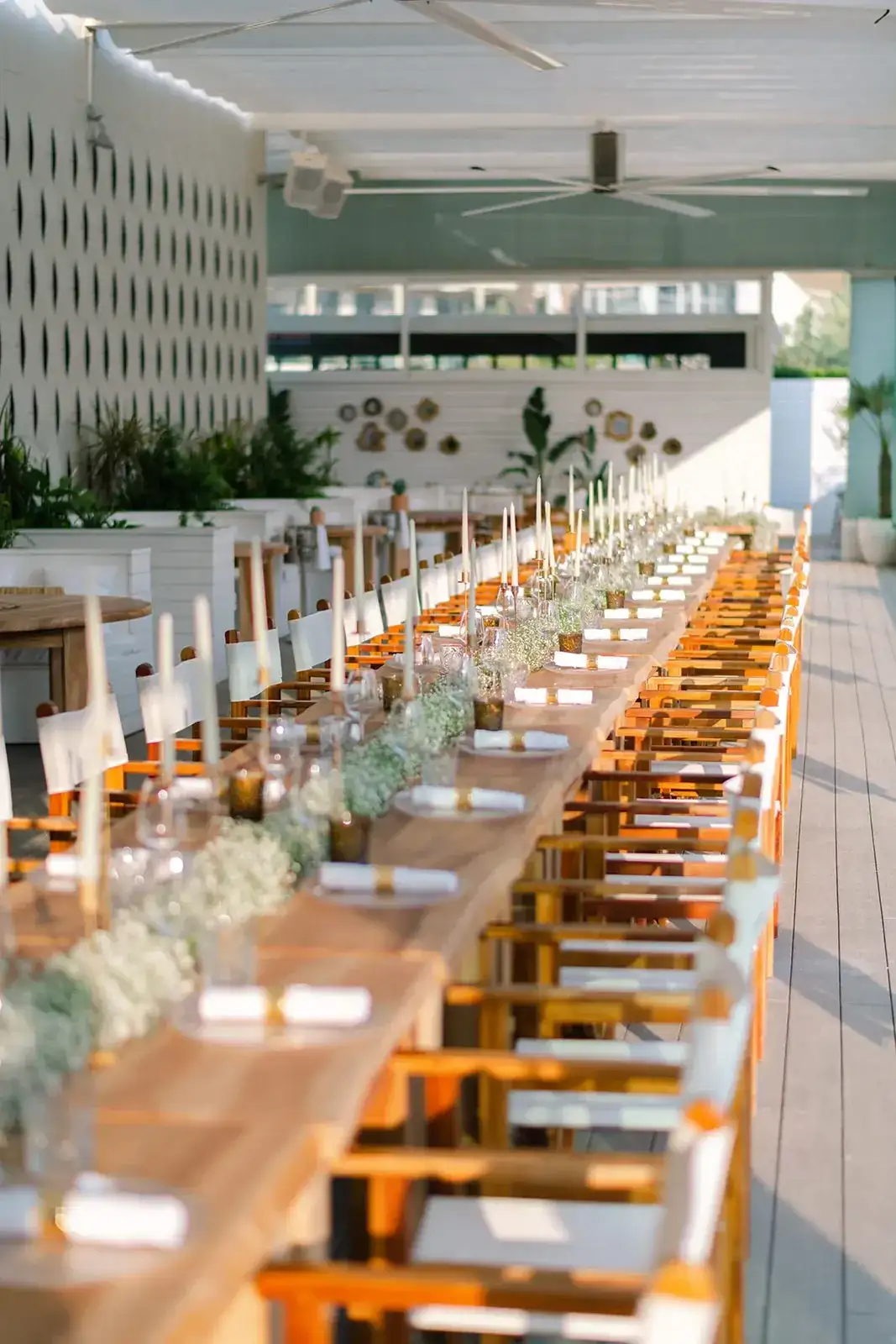 A long wooden table and orange chairs on a white terrace