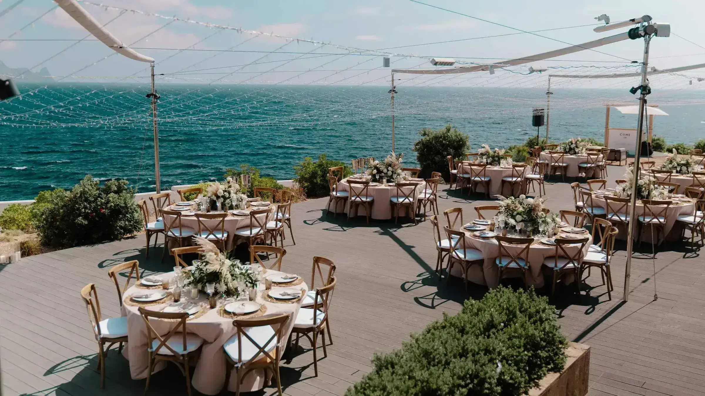 7Pines Resort Ibiza: Clifftop terrace set with round dinner tables under shade sails above the sea