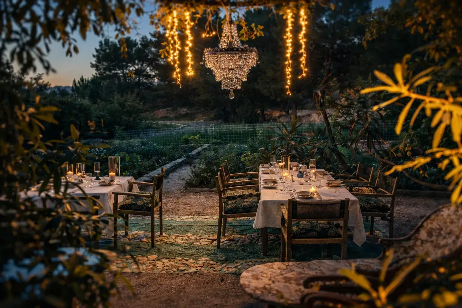A mi Manera: Garden dining tables with a chandelier and light strings hung in the trees at dusk