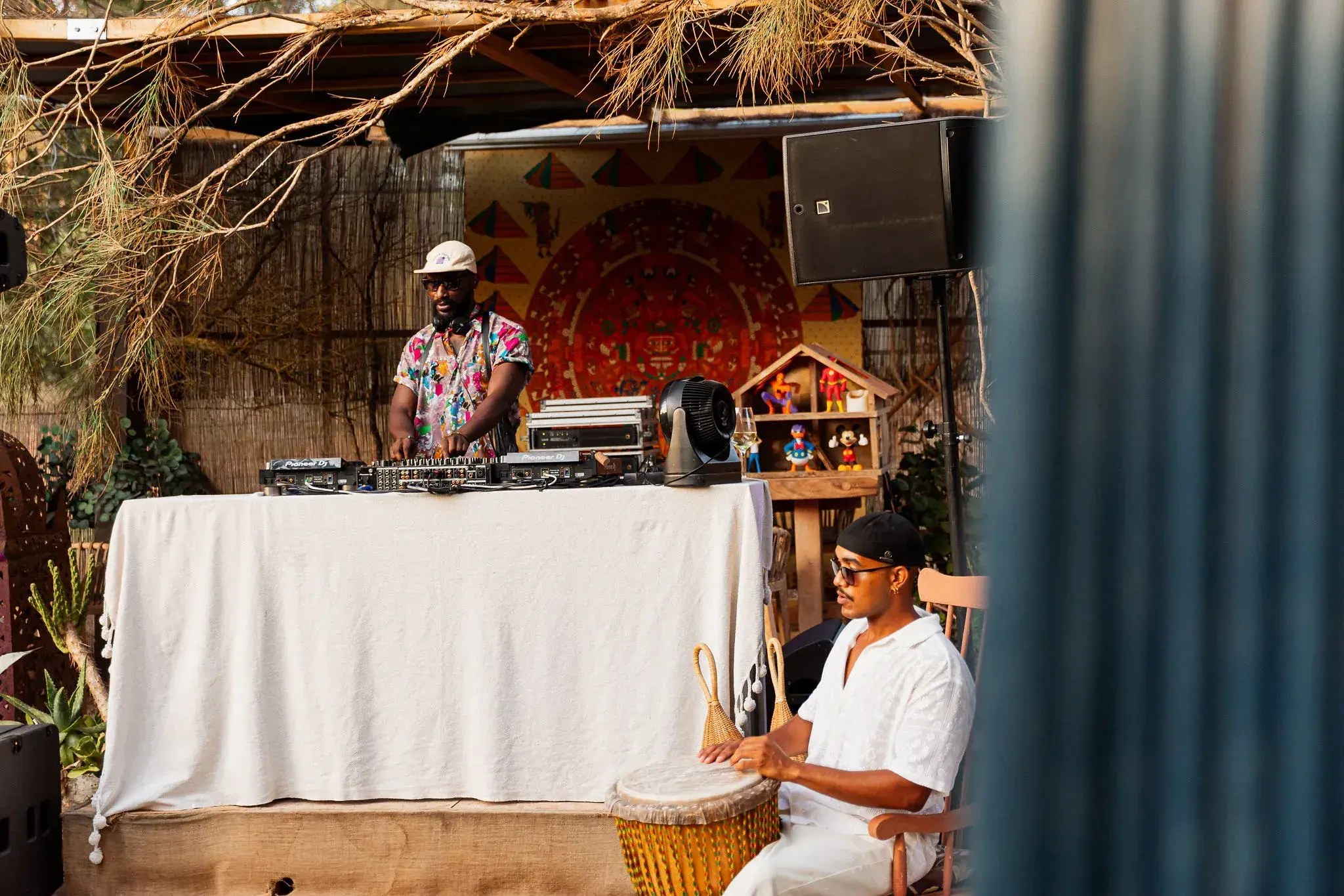 A mi Manera: DJ and percussionist set up under a reed canopy