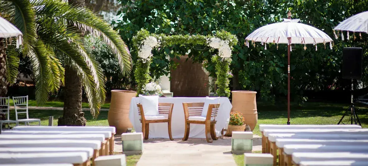 Agroturismo Atzaró: Ceremony in the palm garden with white benches, parasols and a flower-framed altar