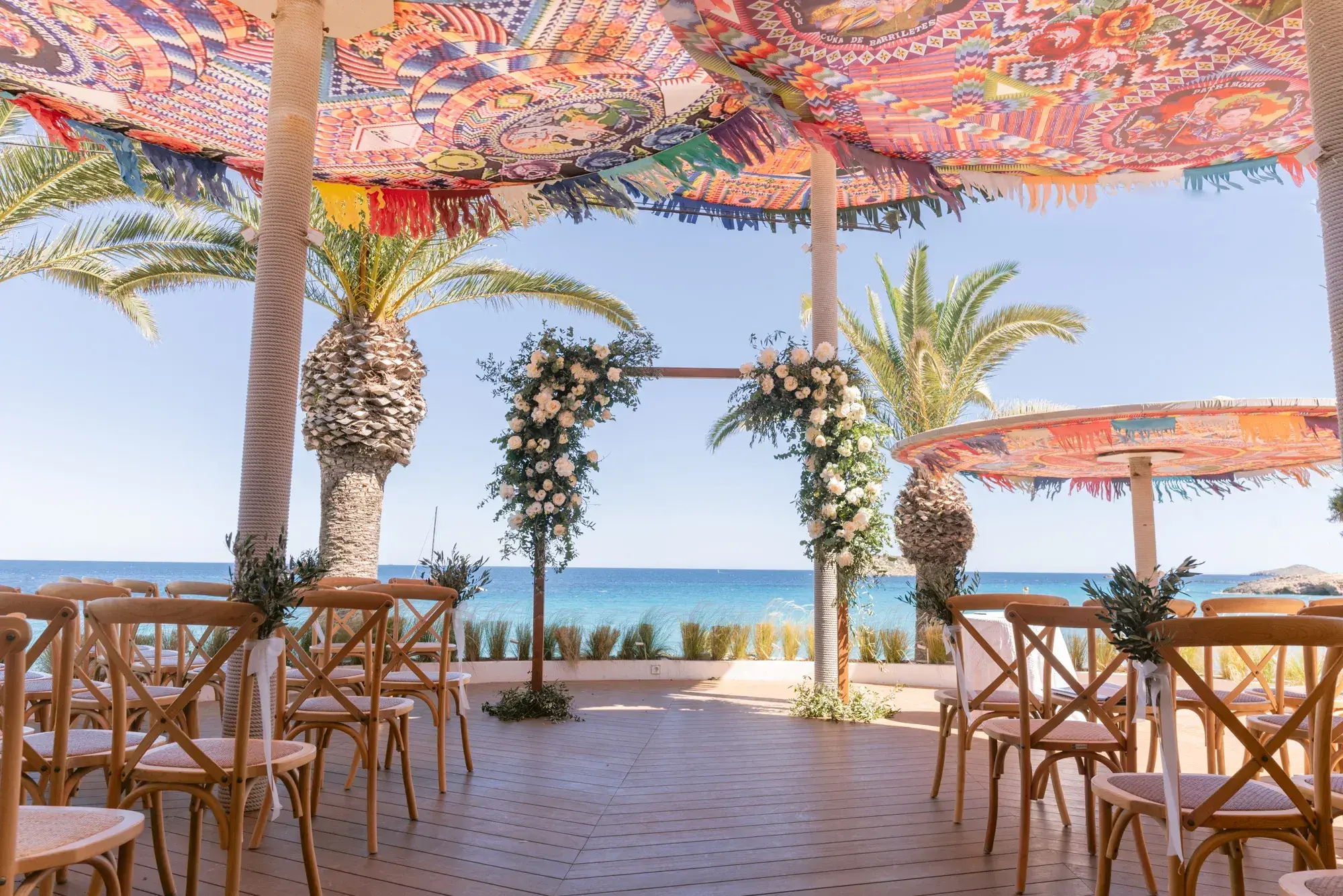 Aiyanna Ibiza: Ceremony set-up on the wooden terrace with floral arch, cross-back chairs and the sea behind