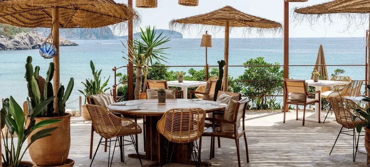 Atzaró Beach: Restaurant terrace with rattan chairs and palm parasols above the sea
