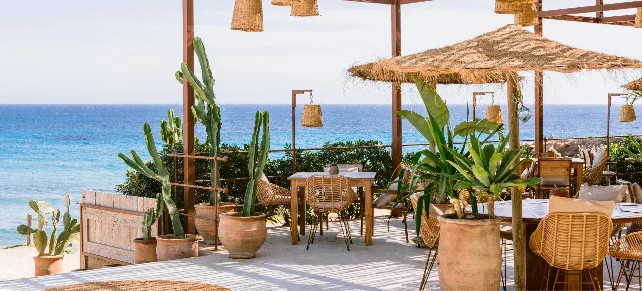 Atzaró Beach: Tables among cacti and potted palms facing Cala Nova