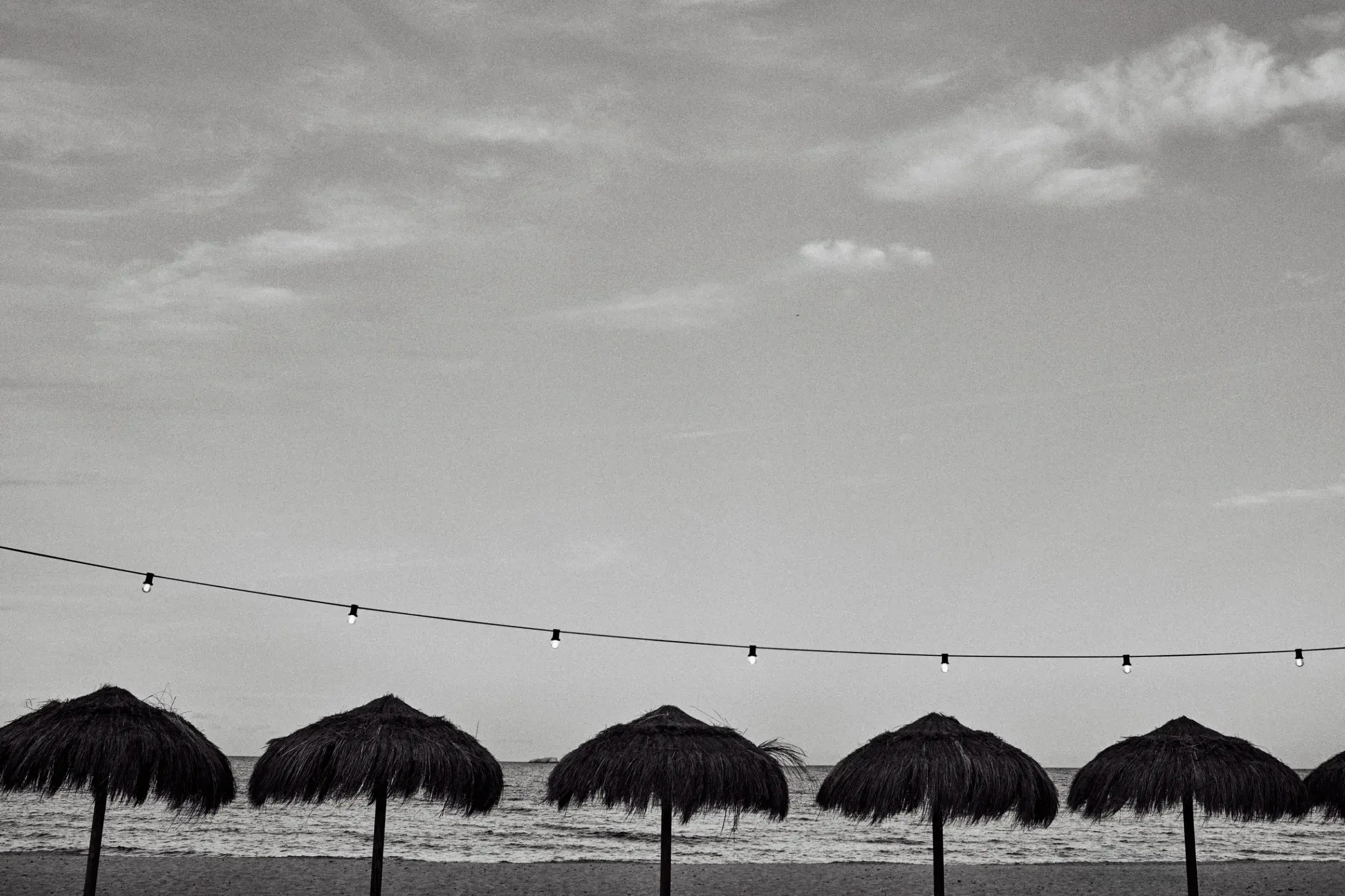 Beachouse Ibiza: Straw parasols on the beach with string lights (black and white)