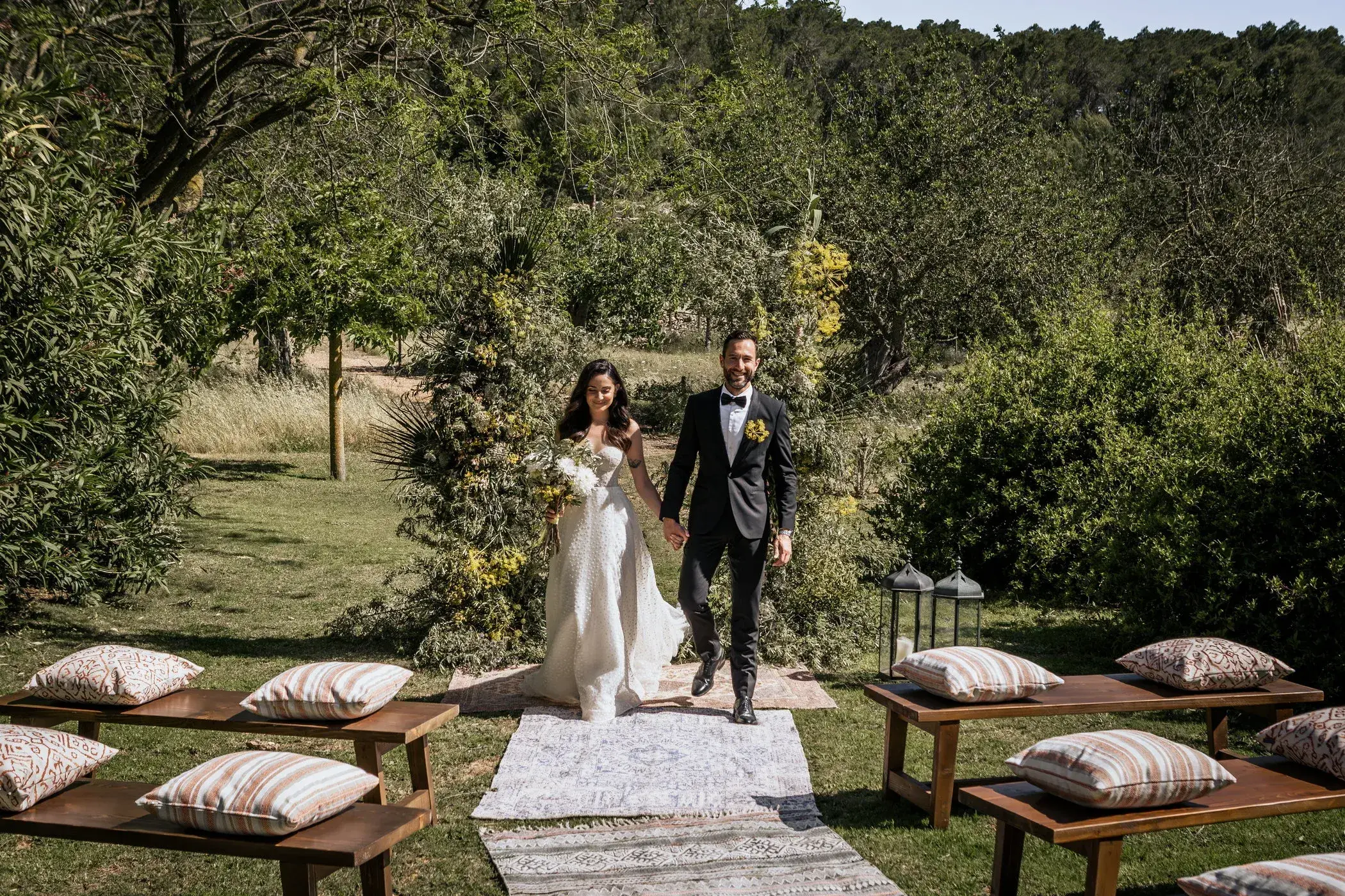 Can Lluc: Couple walking up a rug aisle between benches on the lawn
