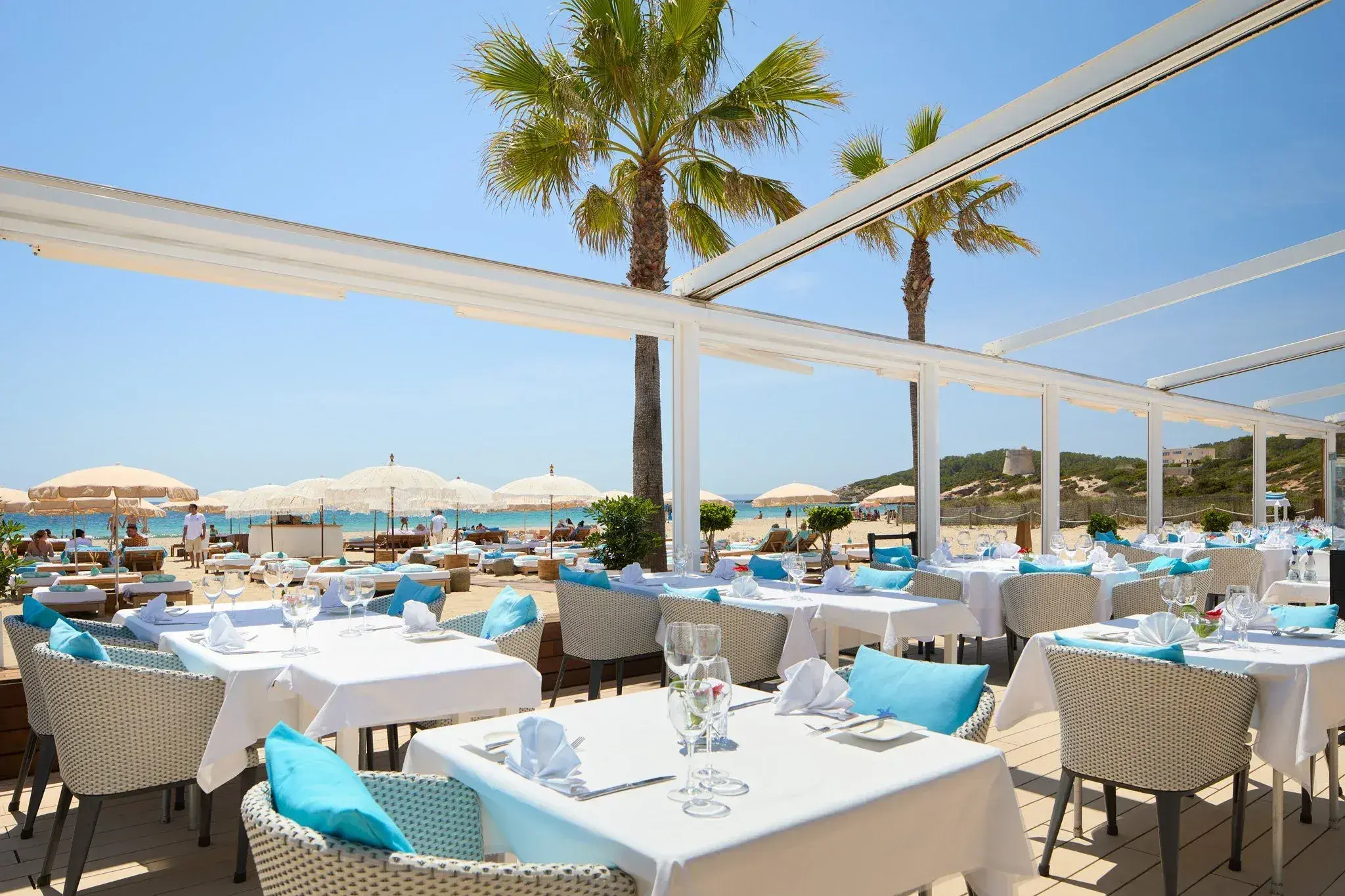 Coco Beach Ibiza: Covered restaurant terrace with white tablecloths and turquoise cushions facing the beach