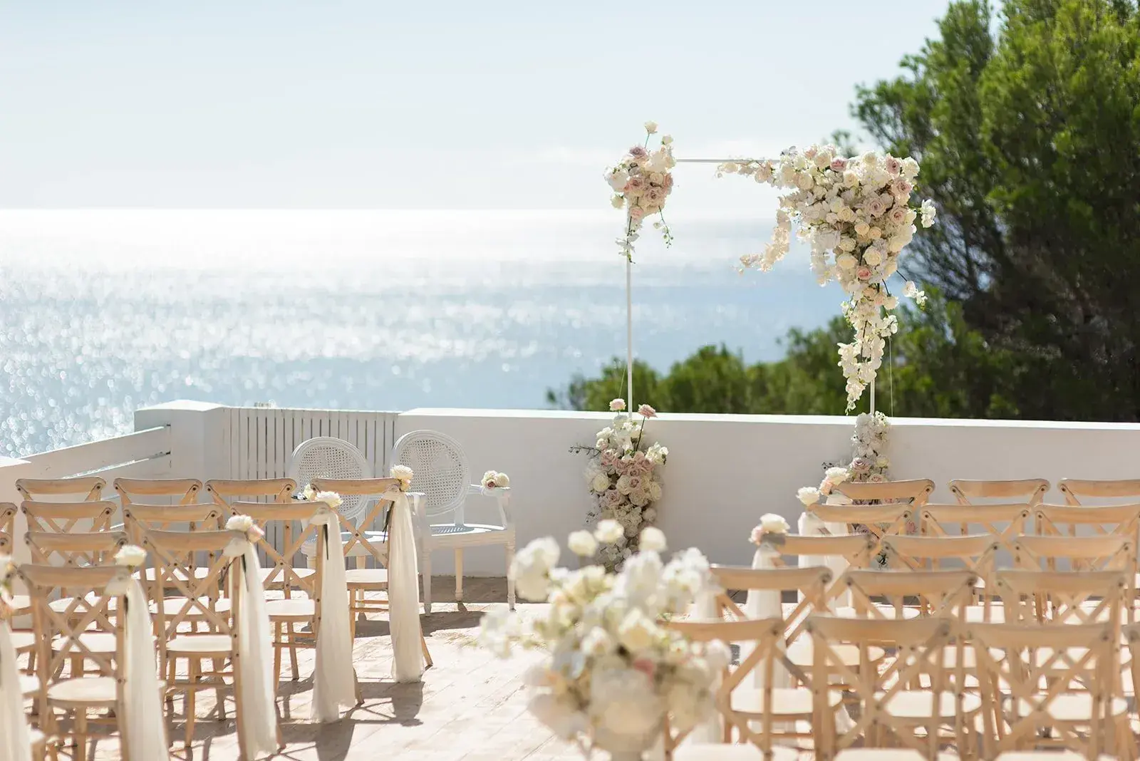 Elixir: Ceremony terrace set with wooden chairs and floral arrangements facing the sea