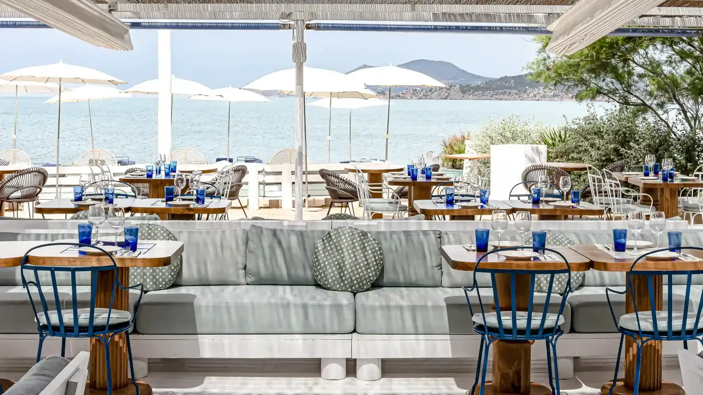 Experimental Beach: Shaded terrace with blue chairs and white umbrellas by the sea