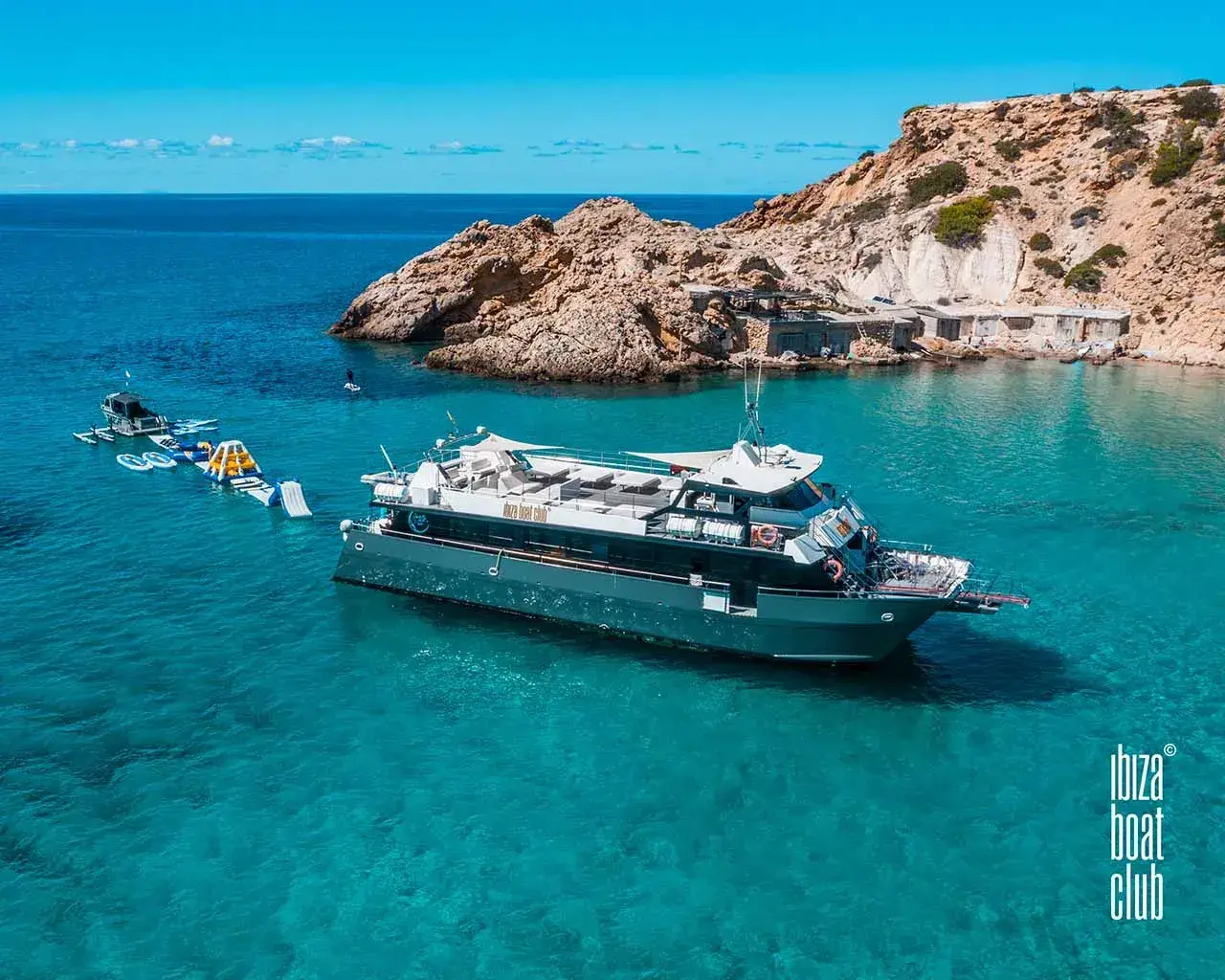 Ibiza Boat Club: Catamaran at anchor beside rocky cliffs with inflatable water toys