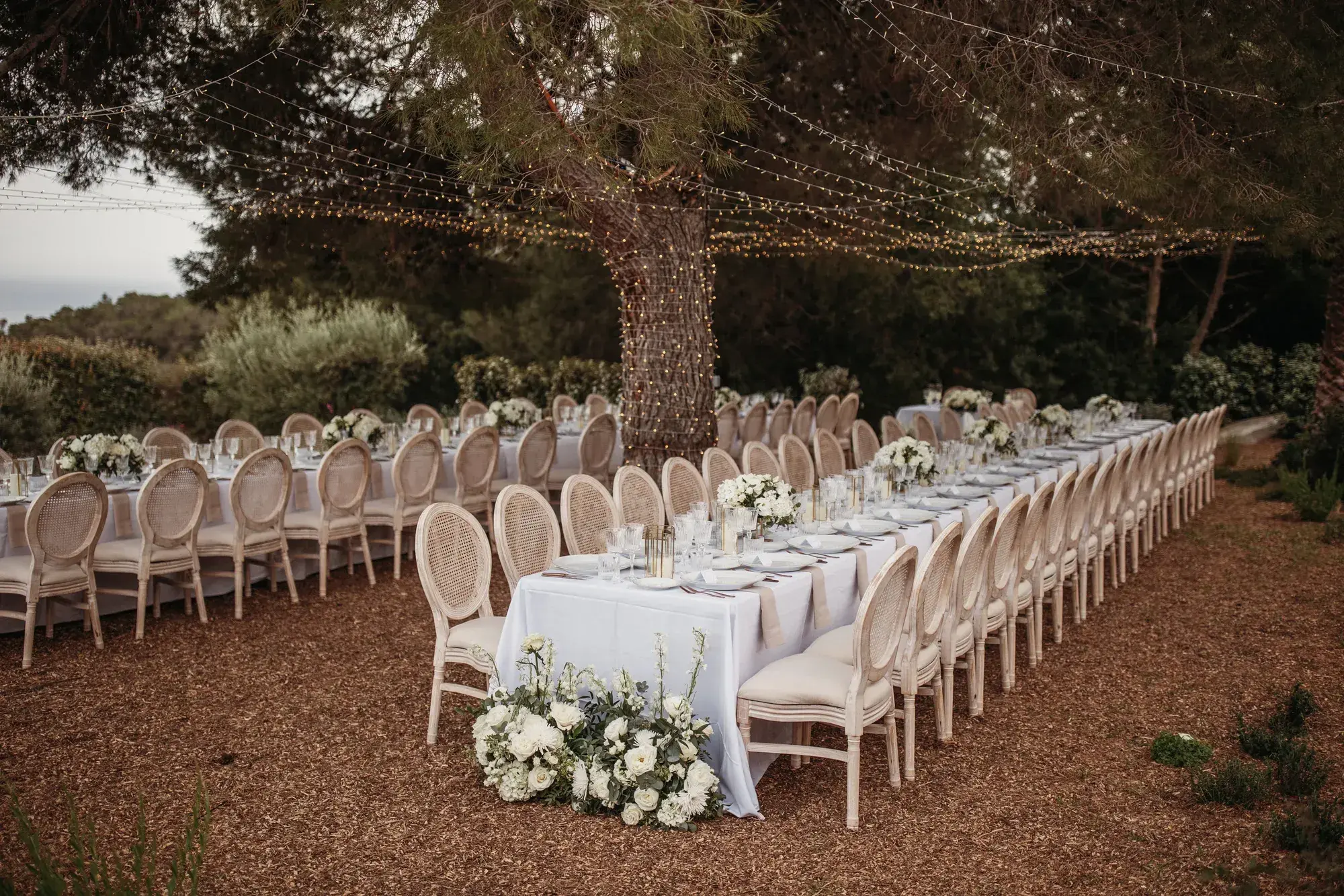 Long white tables under an old pine, a villa wedding in Es Cubells