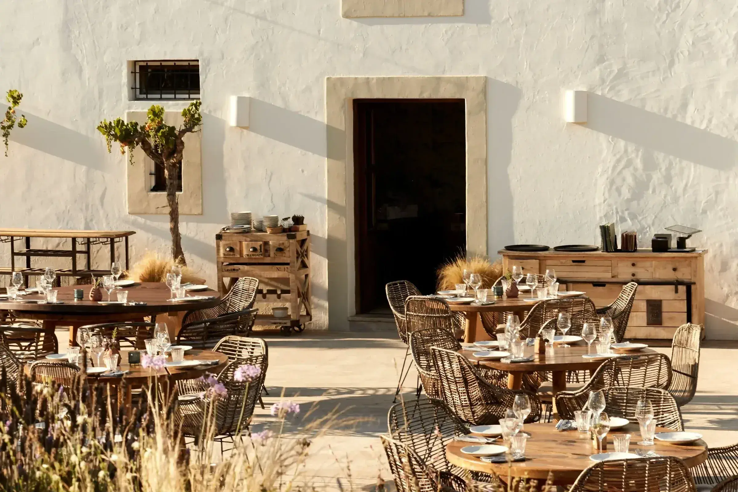 Juntos House: Courtyard tables with wicker chairs against a whitewashed wall