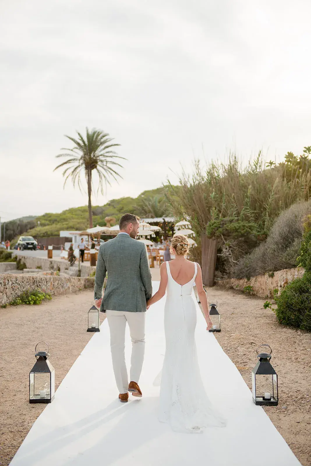 La Escollera: Bride and groom walking along a white aisle lined with lanterns towards the beach
