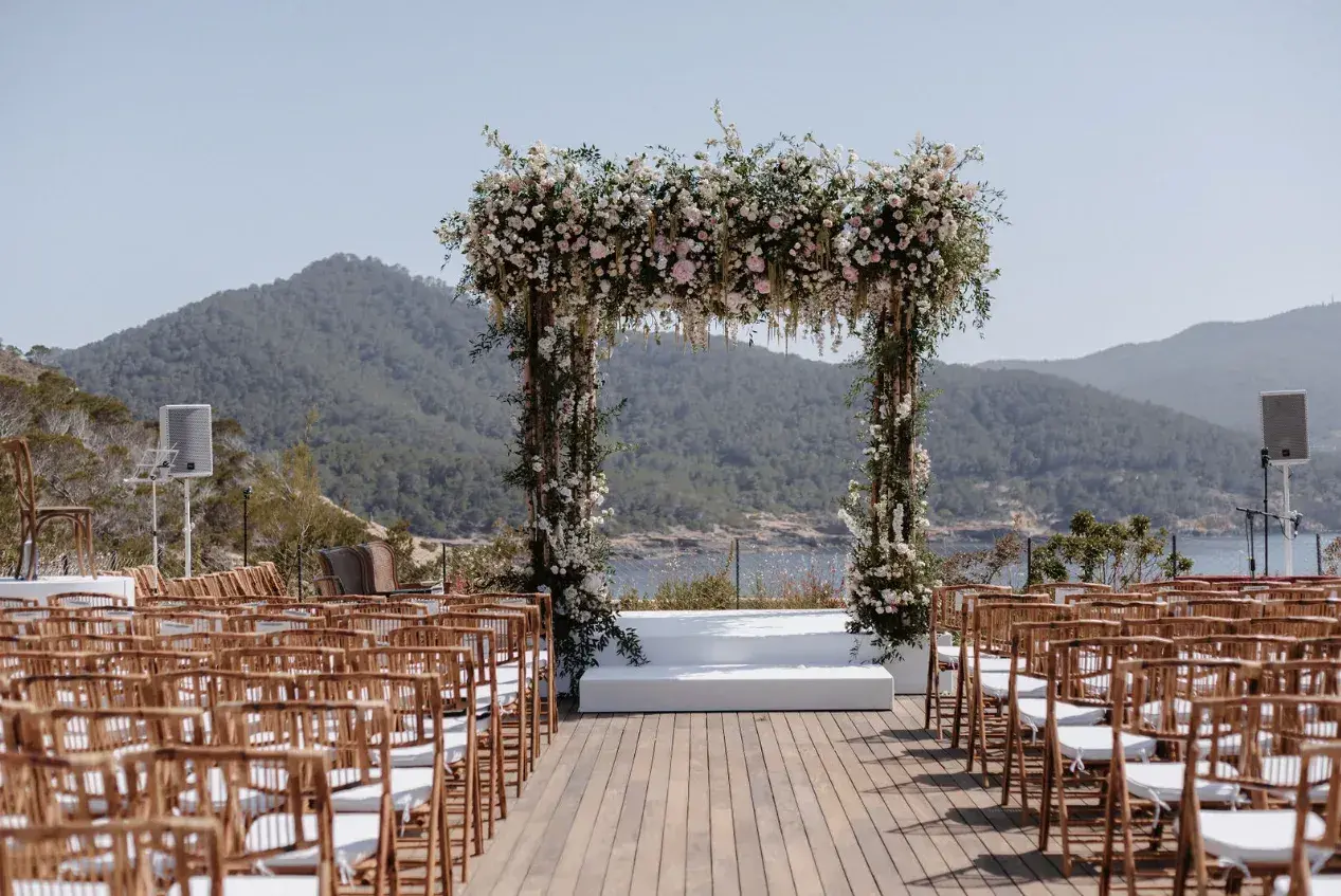 Six Senses Ibiza: Ceremony deck with wooden chairs, a flower arch and the bay and hills behind