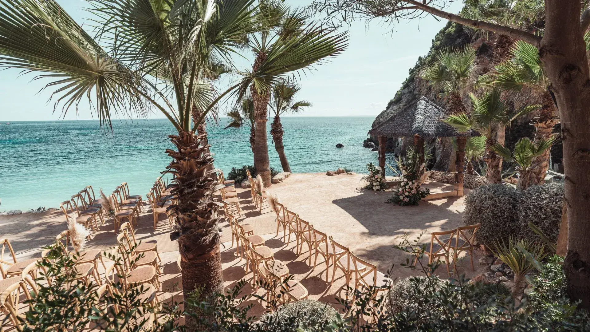 Amante Ibiza: Ceremony seating set out on the terraced steps above the beach with palms and the bay behind