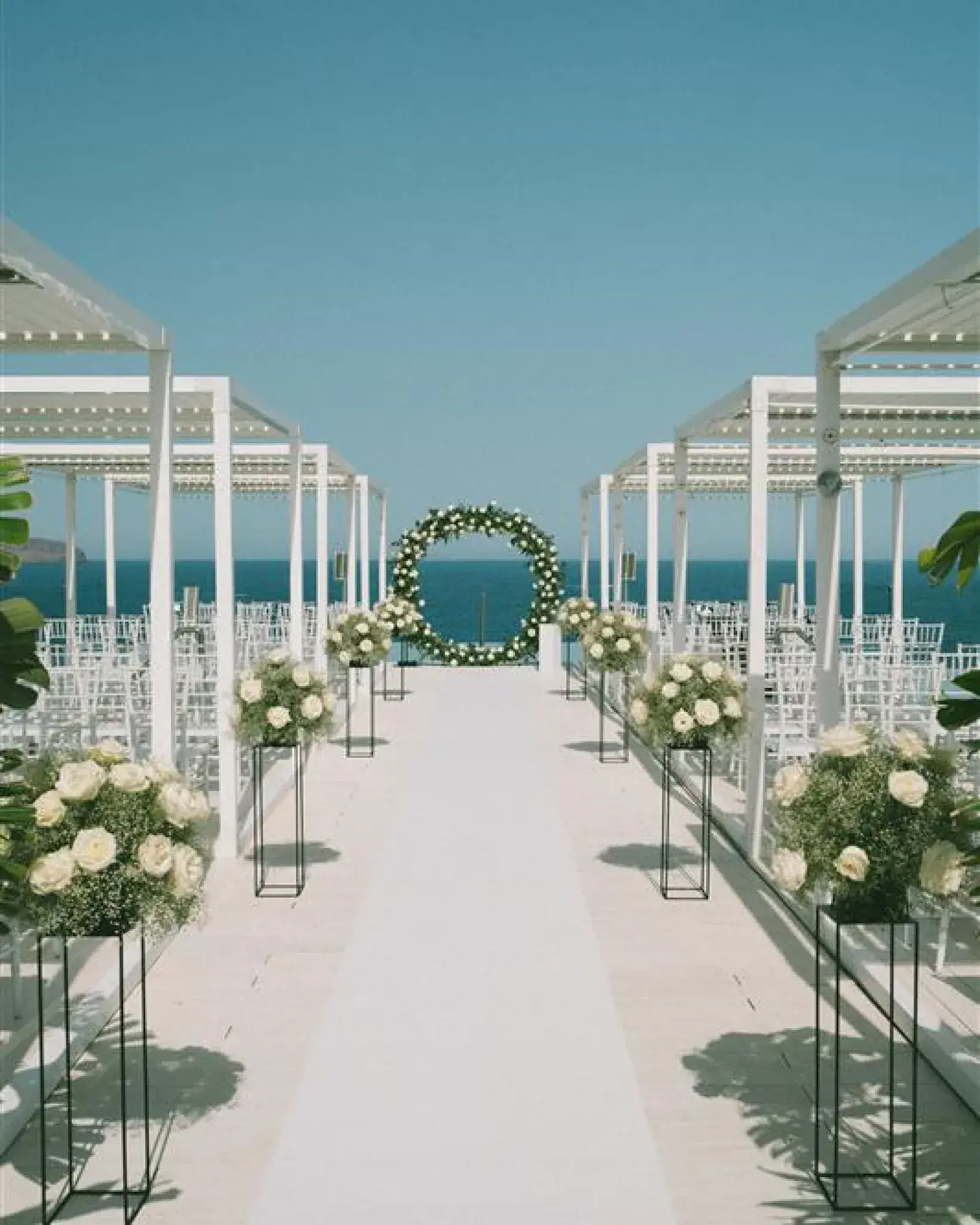 Bless Hotel Ibiza: Ceremony aisle with white flowers under pergolas leading to a floral hoop and the sea