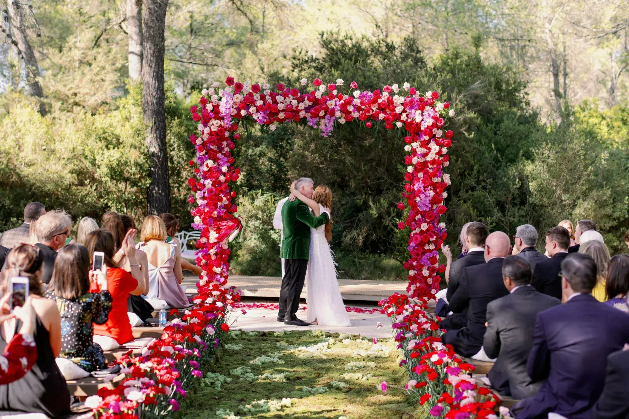 Ca Na Xica: Ceremony under a red and pink flower arch with guests seated either side