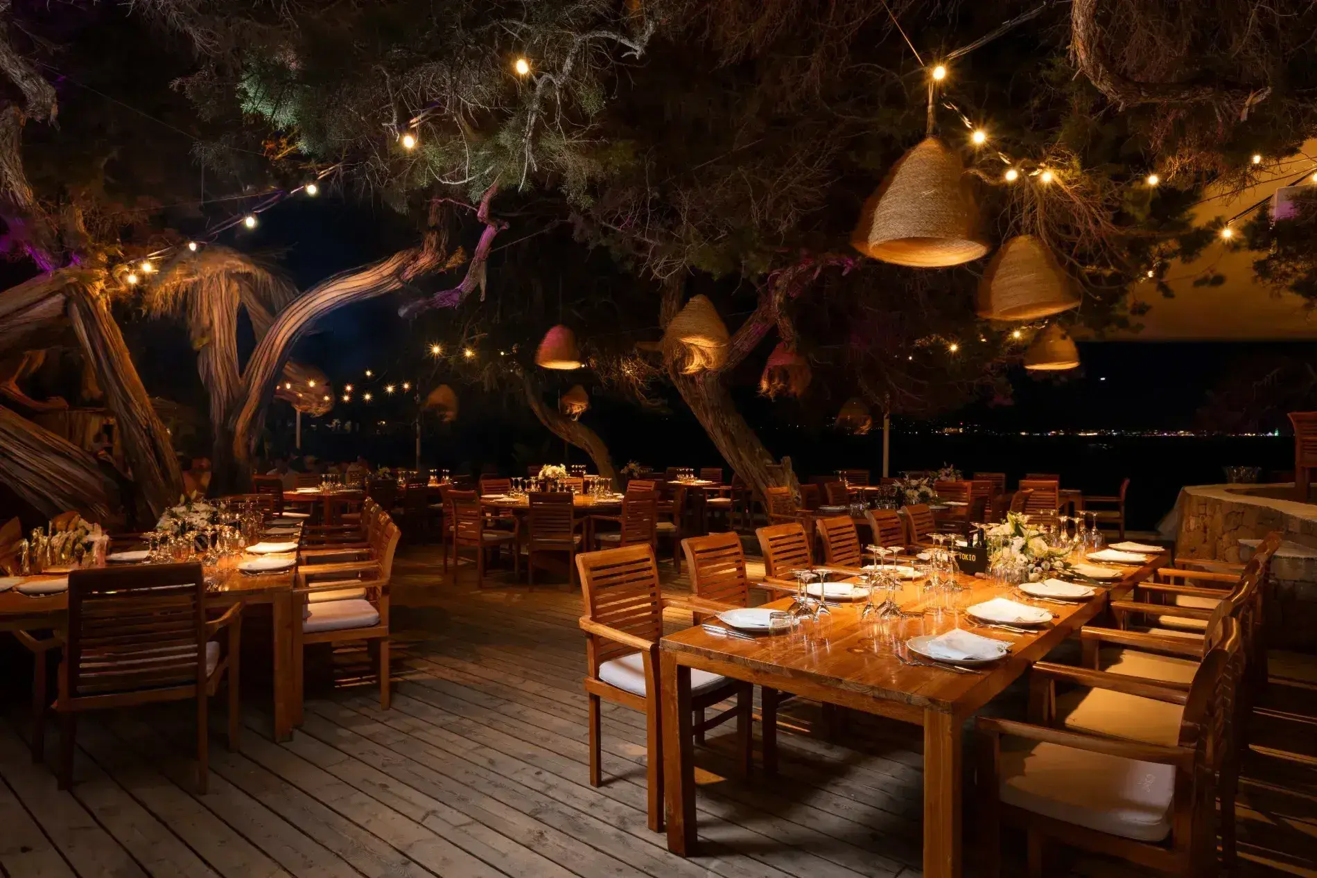 Cala Bassa Beach Club: Restaurant deck under the trees set for a wedding dinner with festoon lights at night