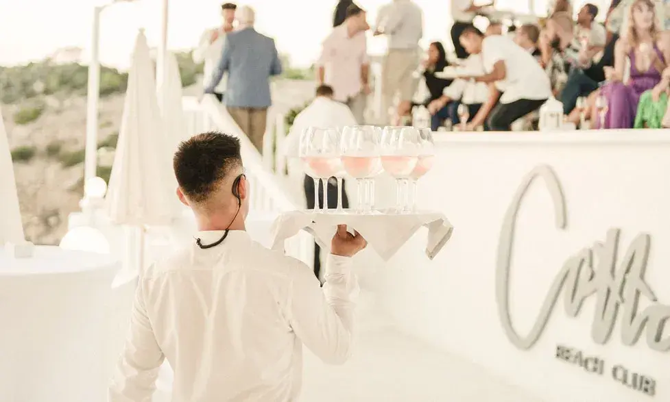 Cotton Beach Club: Event reception with waiter serving drinks by the Cotton Beach Club sign
