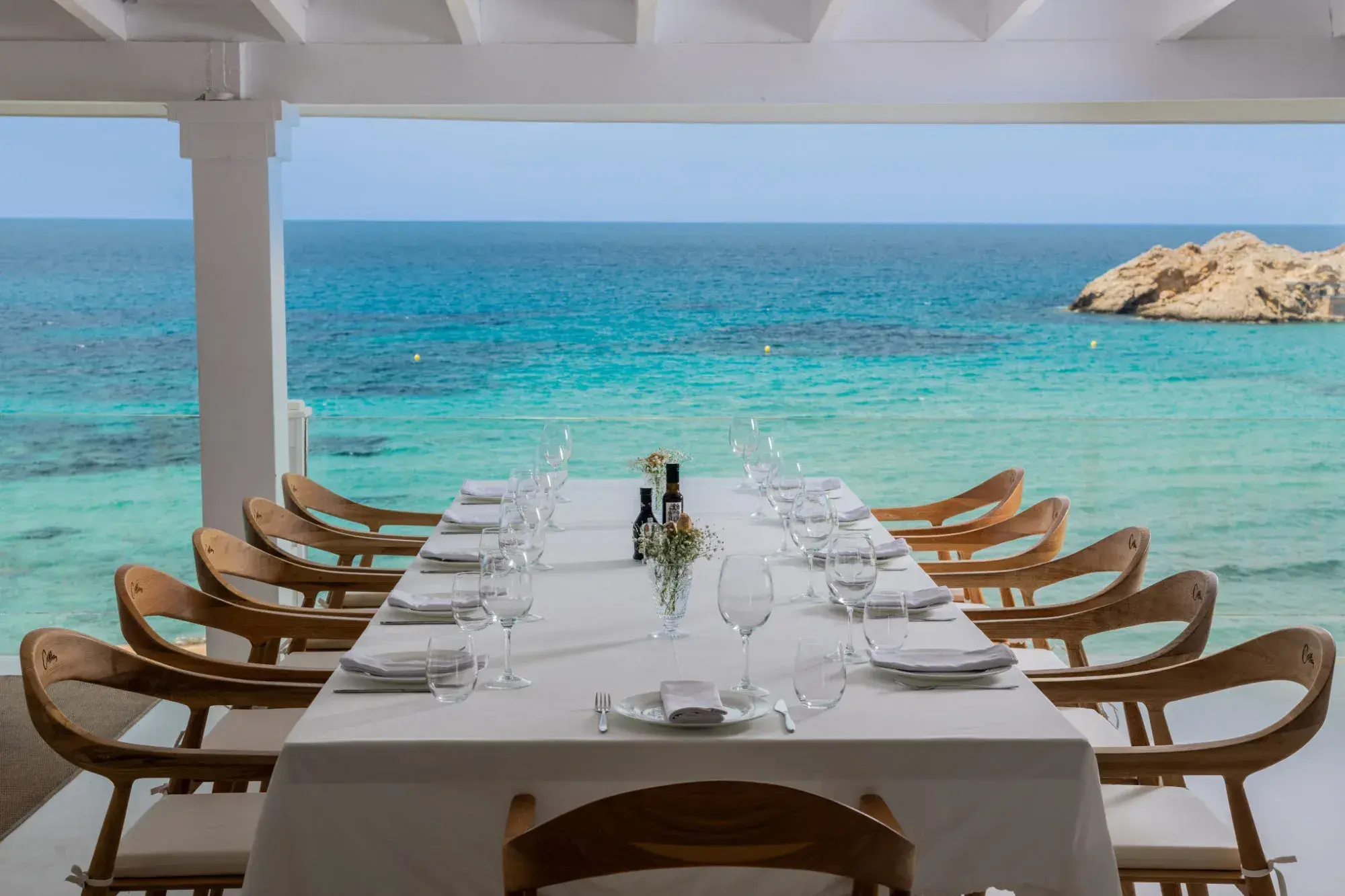Cotton Beach Club: Long table under the white pergola facing the sea and a rocky islet