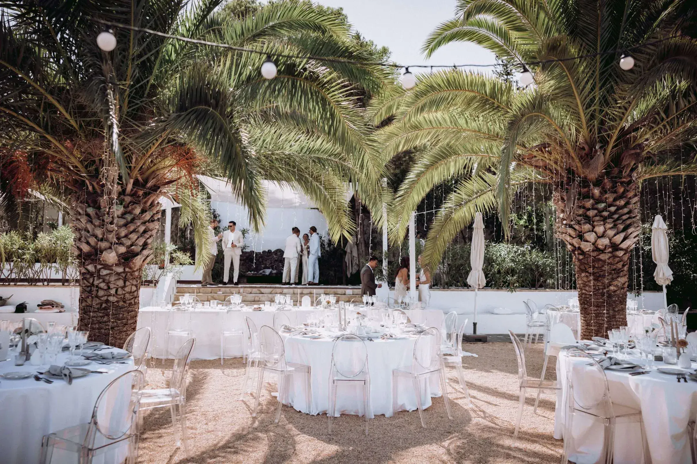Kazamor: Round tables with white linen laid out under the palm trees, with a ceremony area behind