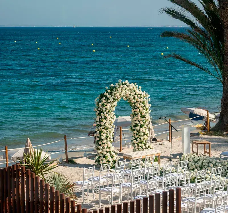 Seahorse Beach Club: Wedding ceremony set-up with white floral arch and white chairs above the beach