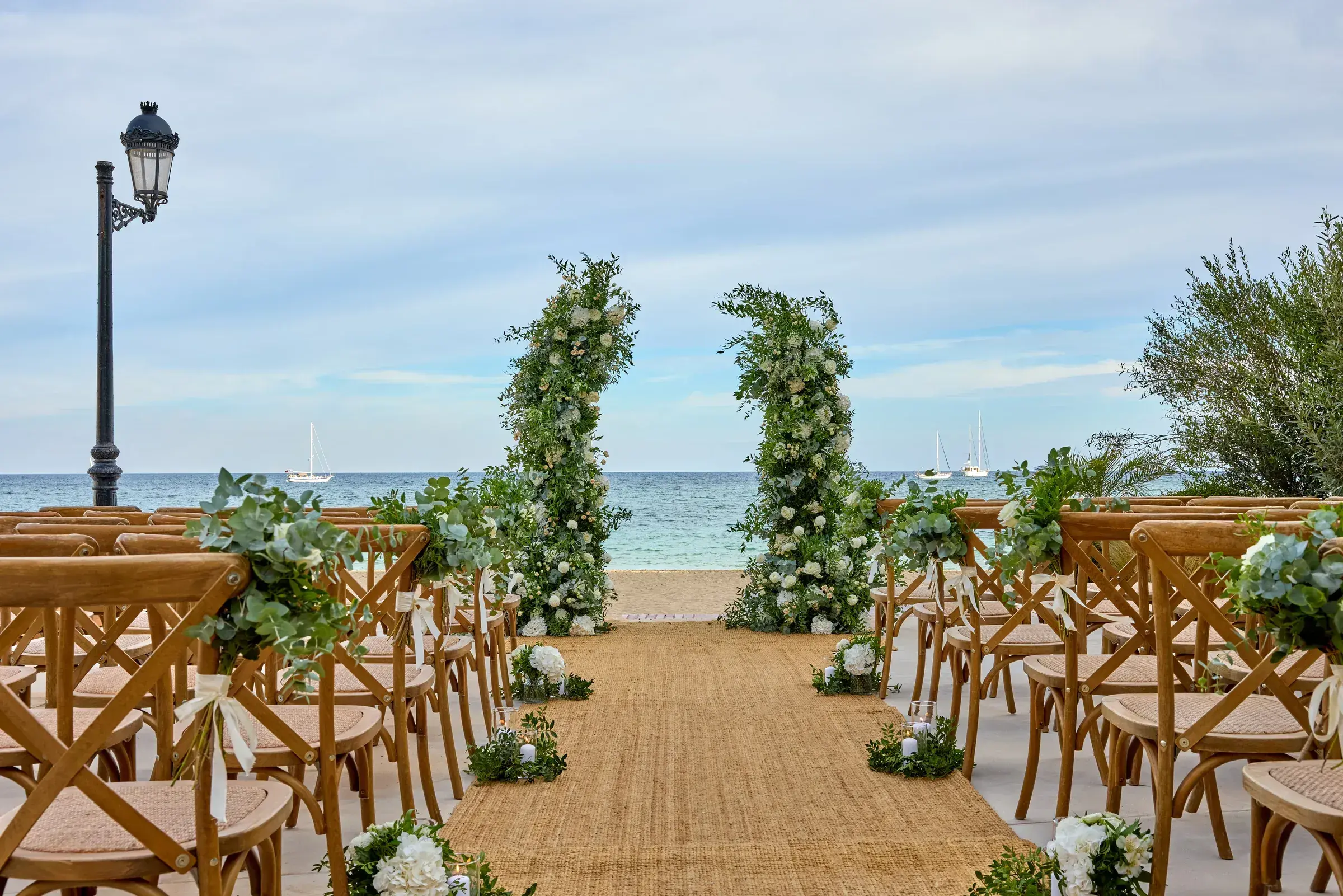 W Ibiza: Ceremony set-up at Yellow Fish: wooden chairs either side of a sisal aisle leading to green floral arches and the sea